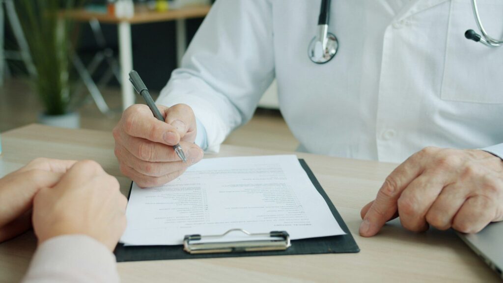 Médico escribiendo en la historia de un paciente durante una consulta